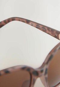 Braune Schildpatt-Sonnenbrille mit einem geschwungenen Rahmen. Der innere Bügel trägt die Kennzeichnungen "CE" und "MADE IN CHINA". Glatte Oberfläche, hochglänzende Ausführung.