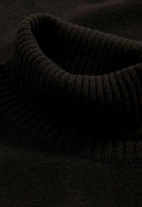 Zwarte gebreide coltrui met een geribbelde kraag en zachte textuur, met een gladde stof die van de kraag naar het lichaam loopt.