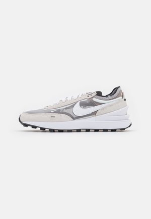 Scarpa da corsa Nike bianca e grigia a profilo basso con tomaia in mesh, swoosh bianco, lacci e suola in gomma nera vista di lato.