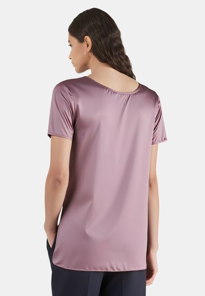 Blusa lilla a maniche corte in tessuto liscio con scollo rotondo e orlo posteriore leggermente più lungo, caratterizzata da un design minimalista.