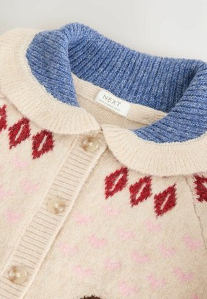 Neulecardigan, jossa on sininen ribbineulekaulus, beige vartalo, jossa on punaisia lehtikuvioita ja vaaleanpunaisia sydämiä. Nappit ovat pyöreitä ja kirkasta muovia.