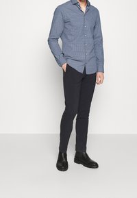 Sinisiä kuvioituja kauluksellisia nappipaitoja, yhdistetty tummiin housuihin ja mustiin nilkkureihin, kapealla leikkauksella ja sileällä tekstuurilla.