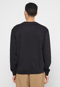 Sweatshirt nero a maniche lunghe con colletto rotondo, texture morbida e polsini a coste, caratterizzato da un fit rilassato e senza loghi o motivi visibili.