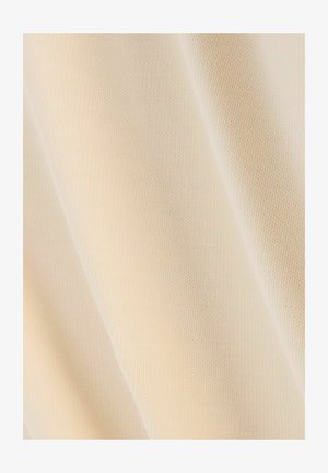 Tela beige con una superficie suave y texturizada, que muestra finos patrones de punto. El material parece ligero y flexible.