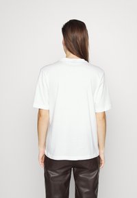 Camiseta de algodón blanca con cuello redondo clásico, mangas cortas y un ajuste relajado. Textura suave, sin patrones ni gráficos visibles.