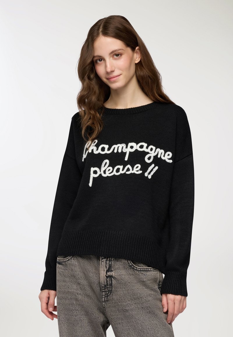 Maglione nero a maglia con testo cursivo bianco "champagne please" sul davanti. Vestibilità ampia con polsini e orlo a costine; texture morbida.