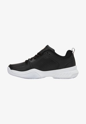 Chaussure de sport noire en cuir synthétique, dotée d'une semelle en caoutchouc blanche, d'un avant arrondi et d'un design à lacets avec des détails perforés.