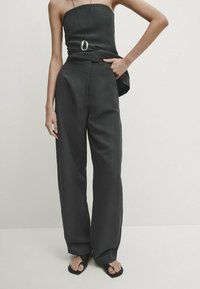 Haut noir sans bretelles associé à un pantalon noir taille haute et ample. La tenue présente une texture lisse et un design minimaliste.