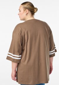 Rjava prevelika majica s kratkimi rokavi z dvema belima črtama. Gladek bombažni material, preprost dizajn in sproščen kroj.