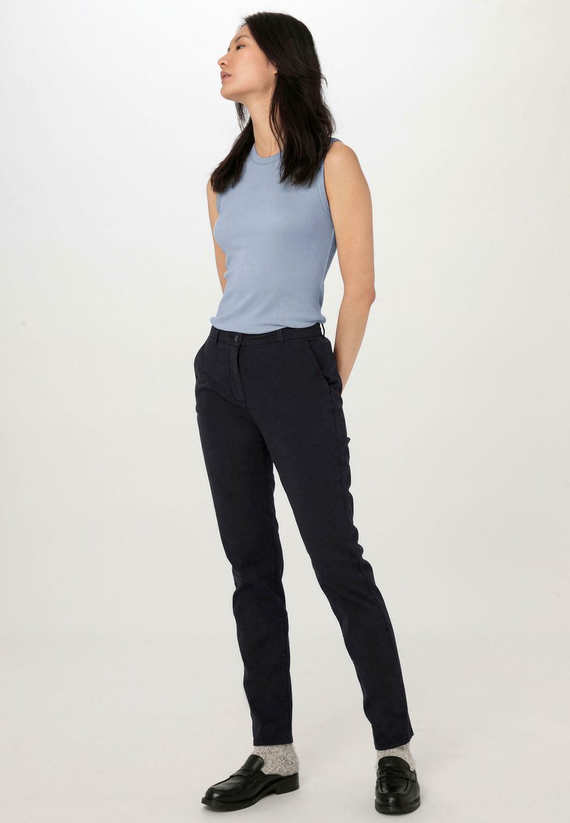 Světle modrý bezrukávový top, tmavě námořnické slim-fit kalhoty, texturované šedé ponožky a černé mokasíny. Jednoduchý design, přiléhavý střih a čisté linie.