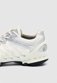 Bijela i siva sportska tenisica s GORE-TEX tkaninom i teksturiranim gumenim potplatom, prikazuje detalje sa strane i stražnjeg dijela.