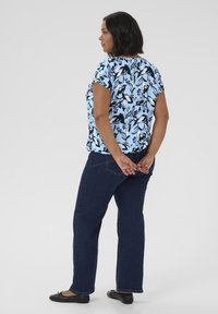 Top florale blu chiaro con dettagli neri, maniche corte e scollatura rotonda, abbinato a jeans dritti blu scuro e ballerine nere.