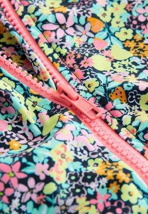 Nærbillede af en koralrød lynlås på stof med et tæt blomster mønster i pastelgule, pink, orange, teal og sorte farver.