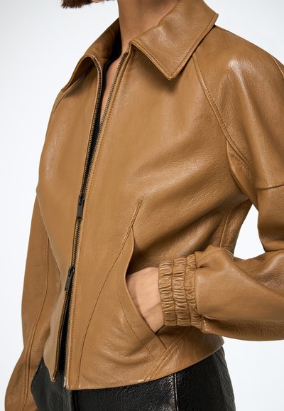 Barna bőrkabát bordázott gallérral és cipzáras záródással. Oldalzsebekkel, testhez szabott szabással és enyhén rövidített kialakítással rendelkezik.