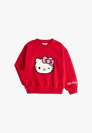 Sweat-shirt rouge à manches longues avec visage de Hello Kitty faisant un clin d'œil et nœud rose sur le devant, et texte "Hello Kitty" brodé sur le poignet de la manche.