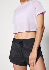 Vaaleanlila lyhyt verkkopaita pyöreällä kaula-aukolla, yhdistettynä mustiin shortseihin, joissa on nauhavyötärö ja hienovaraiset pystyraitat.