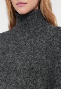 Pulôver de gola alta cinza escuro feito de um tecido de malha texturizada, apresentando um colarinho alto e uma aparência suave e felpuda.