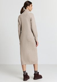 Robe tricotée beige longue avec un col haut, des poignet et un ourlet côtelés, portée avec des bottines noires en cuir et des chaussettes à motifs.