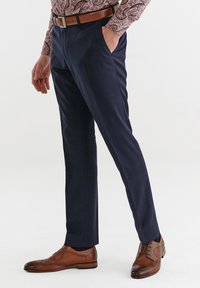 Granatowe, dopasowane spodnie w delikatny wzór w kratkę, zestawione z brązowym skórzanym paskiem i brązowymi butami typu wingtip. Gładka tekstura materiału.