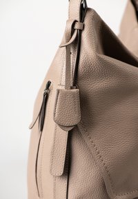 Close-up van een beige leren handtas met een zichtbare rits en een klein leren label waarin "aunts & uncles" is geperst.