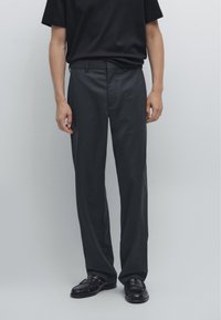 Svarta skräddarsydda byxor i mjukt tyg, med rak ben design och en enkel midja. Stylad med svarta loafers.