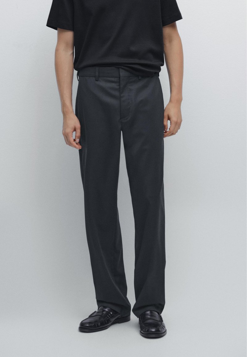 Svarta skräddarsydda byxor i mjukt tyg, med rak ben design och en enkel midja. Stylad med svarta loafers.