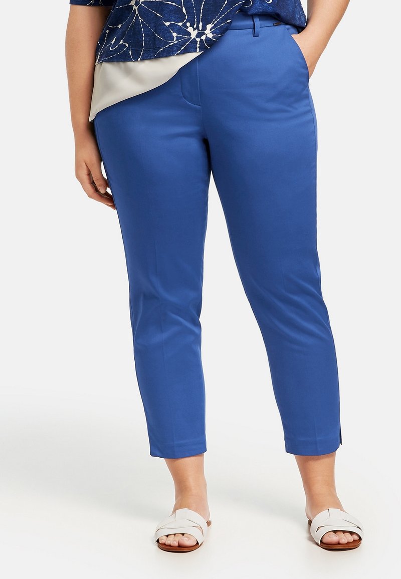 Modré kalhoty vyrobené z hladké tkaniny, užší střih, střední výška pasu, boční kapsy a lem končící těsně nad kotníkem. V kombinaci se světlými sandály.