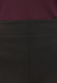 Schwarze Hosen zeichnen sich durch eine glatte Textur und eine maßgeschneiderte Passform aus, mit einem kontrastierenden burgunderfarbenen oberen Abschnitt. Einfaches Design mit klaren Nähdetails.