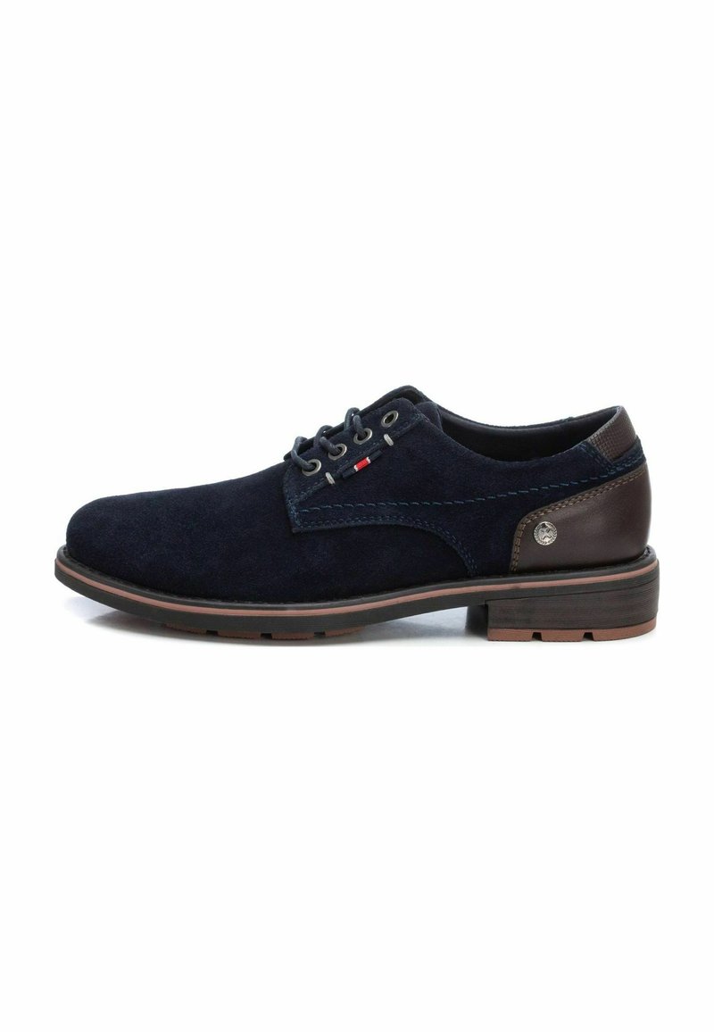 Zapatos de ante azul marino con detalles en cuero marrón, ojales grises y suela a rayas marrones. Presenta costuras azules y un logo decorativo.