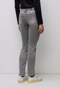 Smalpassade grå jeans i denim med två bakfickor och synliga sömmar. Kombinerade med vita sneakers mot en neutral bakgrund.