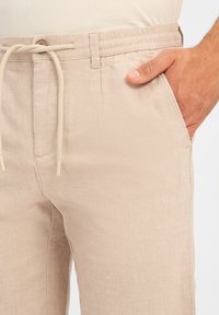 Beige cotton blend pants with a drawstring waist, featuring a textured surface and side pockets.