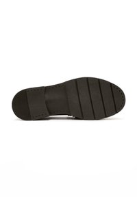 Semelle d'une chaussure de ville noire avec talon texturé, avant-pied rainuré et perforations circulaires le long du bord pour l'adhérence et la durabilité.