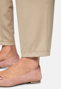 Beige pants with a smooth texture, featuring a straight cut and a hemline. Light pink suede flats with a rounded toe and low heel.