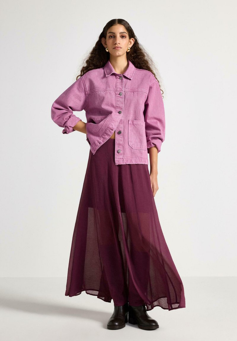 Fuchsia denimjakke med knaplukning og to forlommer, kombineret med en gennemsigtig bourgogne maxi nederdel og sorte ankelstøvler.