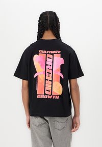 Black cotton t-shirt featuring a colorful graphic on the back with the words "Cultivate Orchid Growth" in bold, vibrant pink and orange hues.