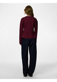 Tamnocrvena uska bluza s dugim rukavima i peplum rubom, uparena s lepršavim tamnim trapericama. Glatka tekstura, minimalistički dizajn.