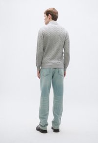 Γκρι πουλόβερ με πλεκτό σχέδιο και ψηλό γιακά, συνδυασμένο με ανοιχτό μπλε τζιν σε άνετη, χαλαρή γραμμή. Το ύφασμα φαίνεται υφή και μαλακό. Μαύρα παπούτσια χωρίς κορδόνια.