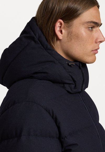 Dark navy puffer jacket with a high collar and hood. Features a smooth texture, button closure, and subtle quilted detail on the fabric.