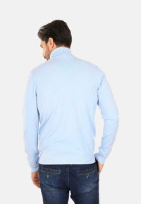 Maglione a collo alto di colore azzurro chiaro con texture a coste e maniche lunghe, abbinato a jeans blu scuro con tasche posteriori.