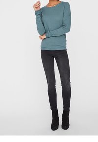 Směs zelenomodrého dlouhého rukávu s texturou, spárovaná s tmavými úzkými džínami a černými kotníkovými botami. Svetr má kulatý výstřih a žebrovaný lem.