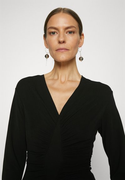 Μαύρο φόρεμα με μακριά μανίκια και βαθύ V-ντεκολτέ, με μαζεμένη υφή στο μπροστινό μέρος. Περιλαμβάνει ασημένια κρεμαστά σκουλαρίκια με στρογγυλές λεπτομέρειες.