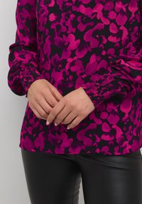 Lilla bluse med blomsterprint, lange ærmer, samlede manchetter og en blød tekstur, parret med sorte læderbukser.