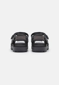 Dark gray sandals featuring a textile upper, adjustable straps, and a textured rubber sole for grip. Minimalistic design with open heel.
