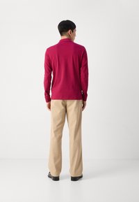 Bordeaux katoenen poloshirt met lange mouwen, gecombineerd met beige broeken. Het shirt heeft geribbelde manchetten en een klassieke kraag.