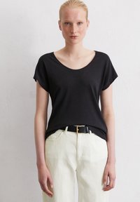 T-shirt noir à manches courtes avec un col rond, associé à un pantalon clair et une ceinture noire avec une boucle dorée.