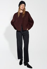 Burgundy cropped cardigan with dropped shoulders and single button closure, paired with straight black jeans and black ankle boots.