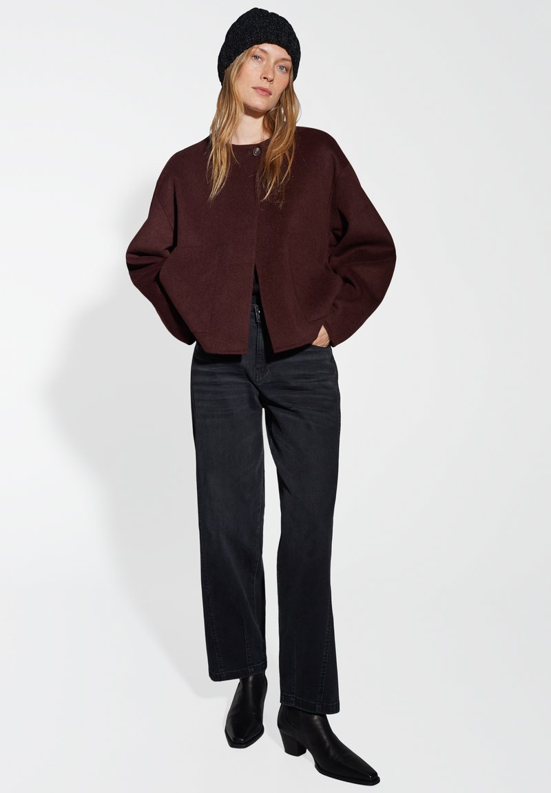 Burgundy cropped cardigan with dropped shoulders and single button closure, paired with straight black jeans and black ankle boots.