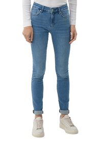 Jean skinny bleu clair taille haute, avec un léger délavage, design à cinq poches et ourlets retroussés, associés à des baskets crème.
