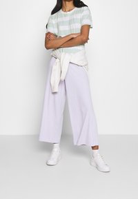 Pruhované zeleno-bílé tričko, spárované se světle purpurovými zkrácenými kalhotami a bílými teniskami. Svetřík uvázaný kolem pasu přidává detail vrstvení.