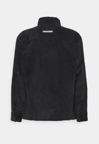 Camicia in velluto a coste nera con colletto, polsini abbottonati e superficie testurizzata. Presenta un piccolo etichetta bianca "PEGADOR" sulla parte posteriore.